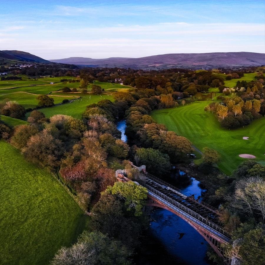 Aerial view of a wooded river valley with a bridge and golf course