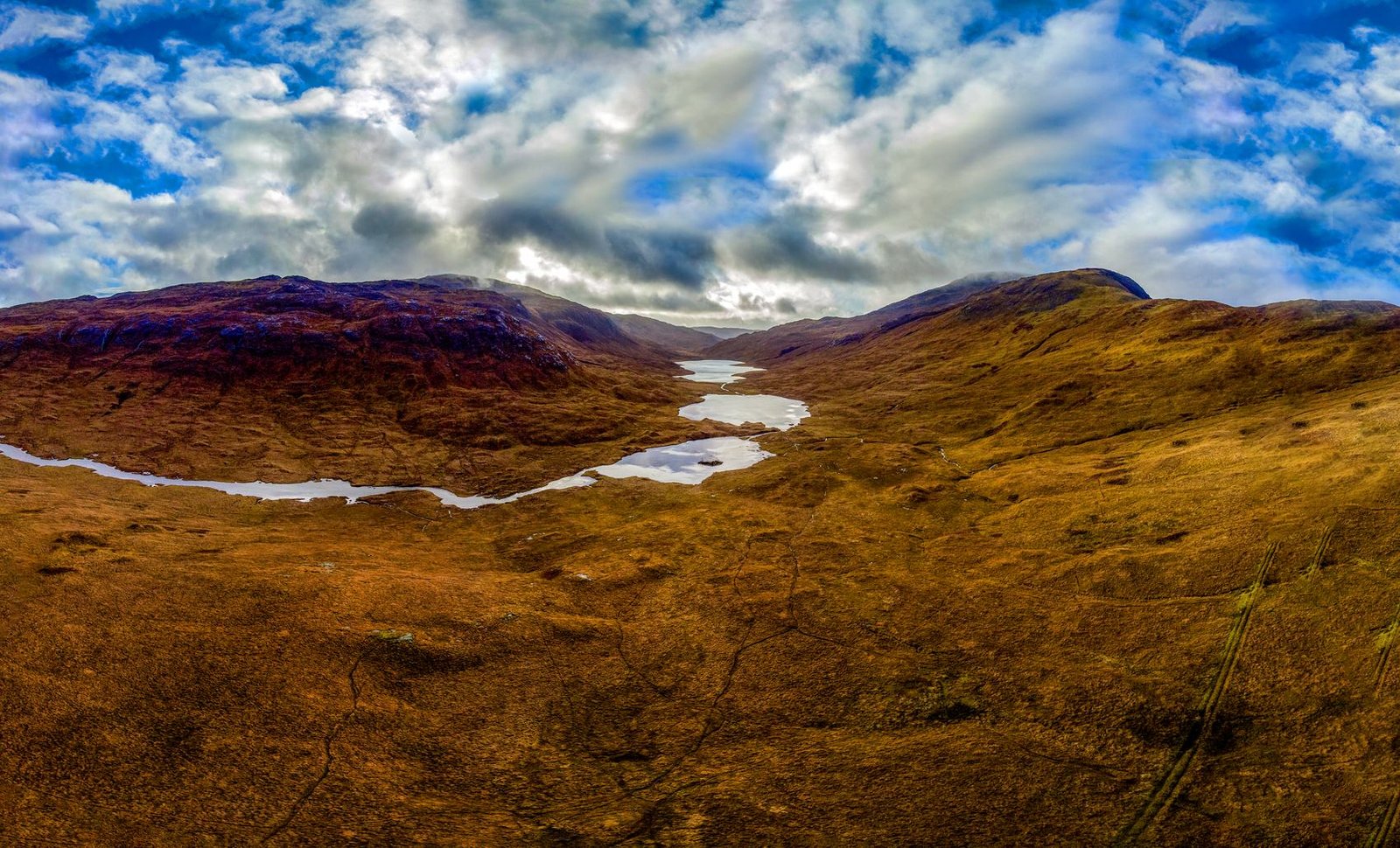 Aerial panorama of Glen More, a moorland valley with small lochs under broken cloud